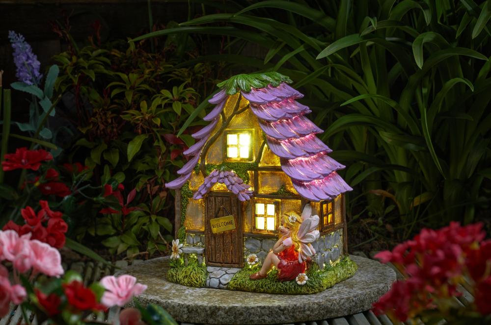 Solar-Feenhaus in Form einer kleinen Waldhütte im Garten stehend, beleuchtet.